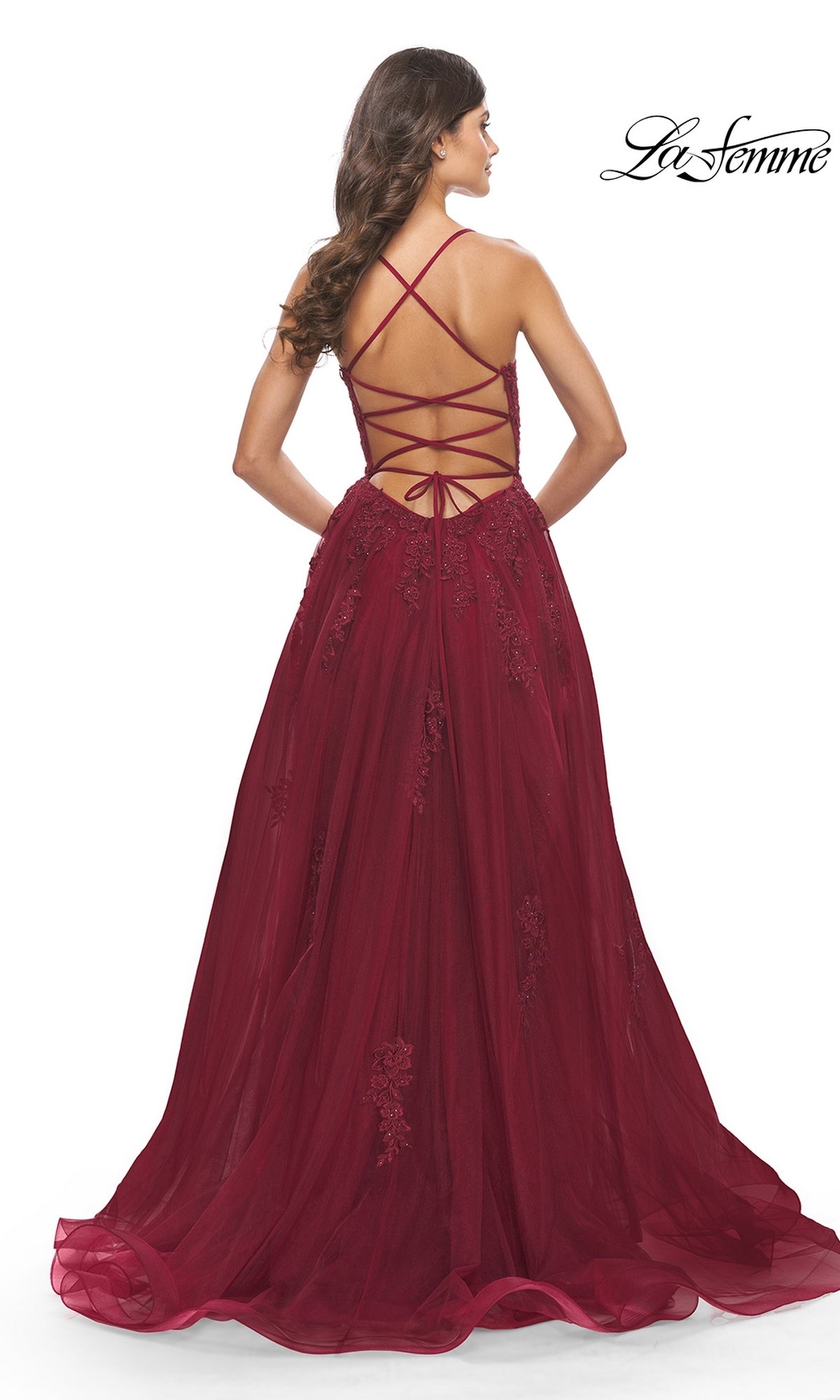 A woman models the La Femme Long A-Line Lace Prom Ball Gown 31135 in burgundy with embroidery and a crisscross lace-up open back, standing against a white background.